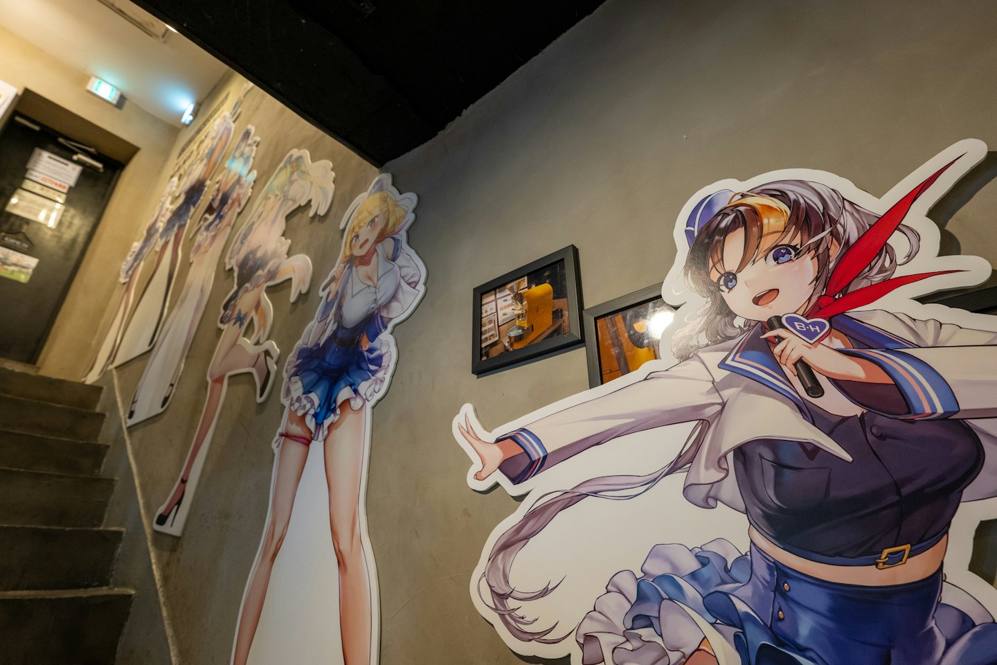 Standee di personaggi anime fiancheggiano una scala di cemento vicino a un'insegna di uscita.
